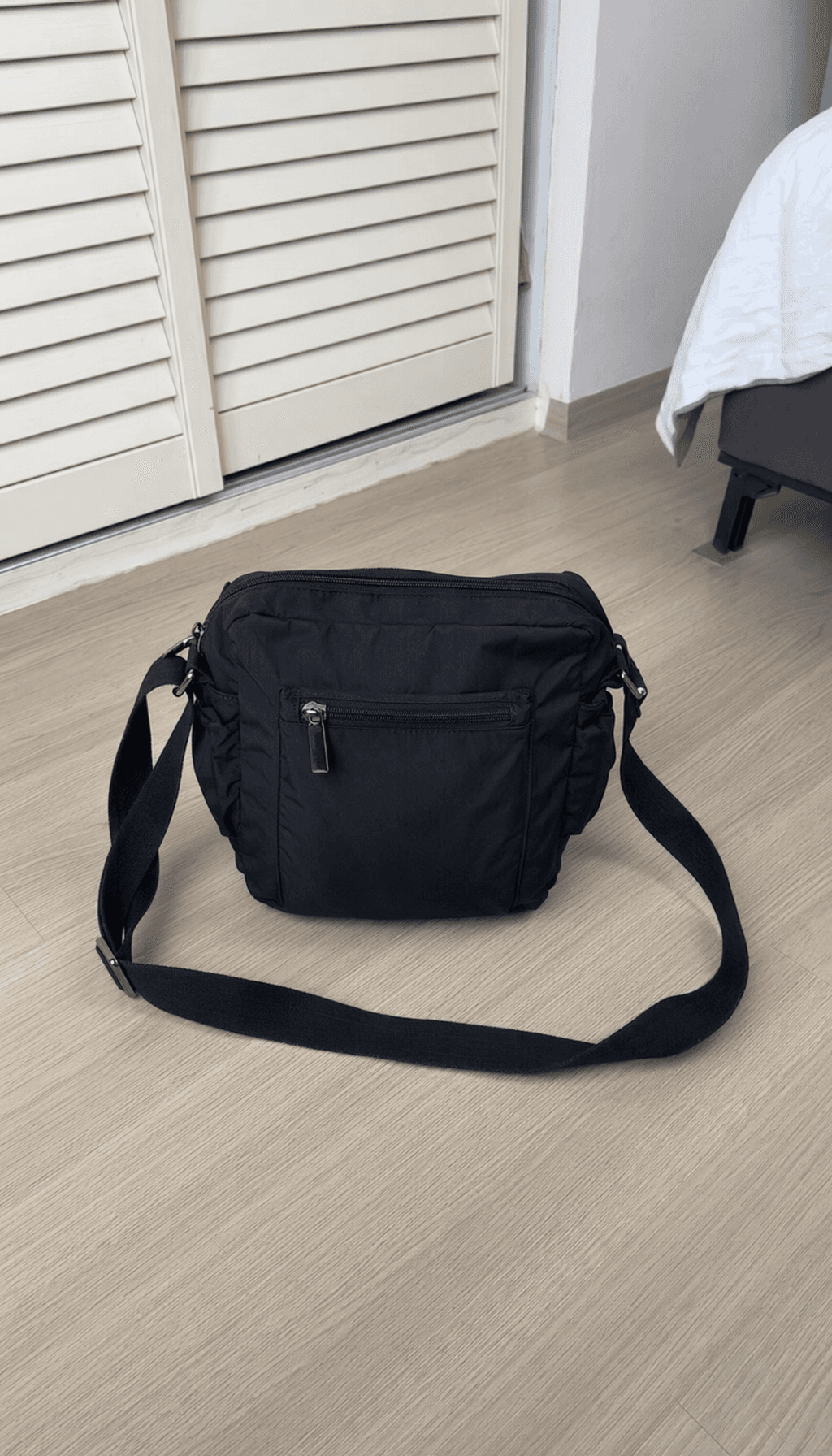 Black crossbody bag photographed on a bedroom floor before cleanup